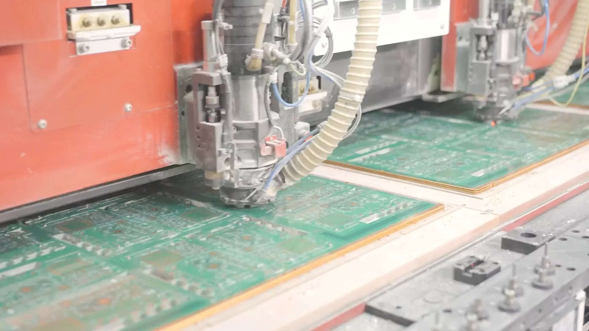 CNC router cutting the profile of a green PCB panel held on the machine table.