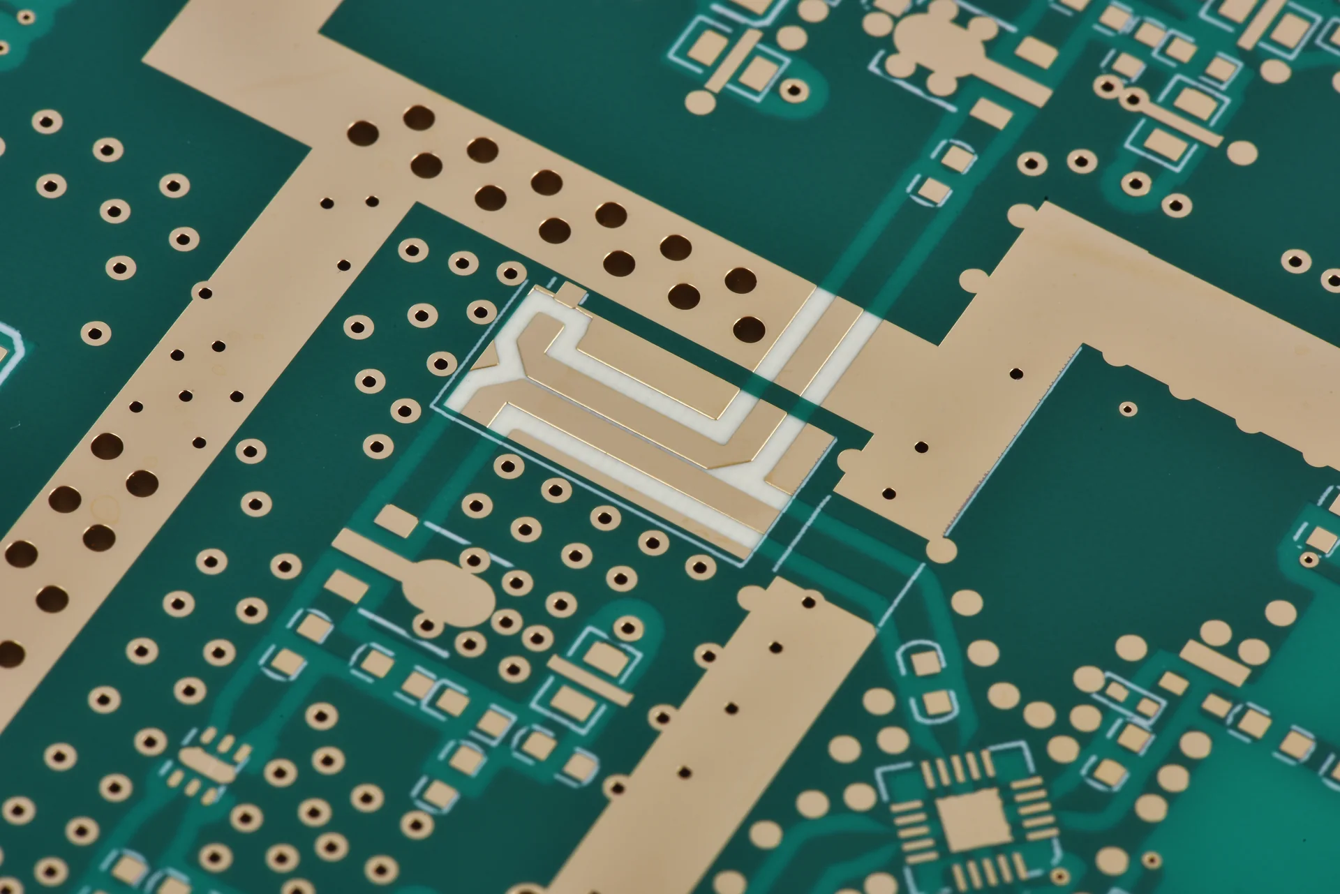 Close-up of a PCB with green solder mask, exposed gold-colored pads and patterned RF copper